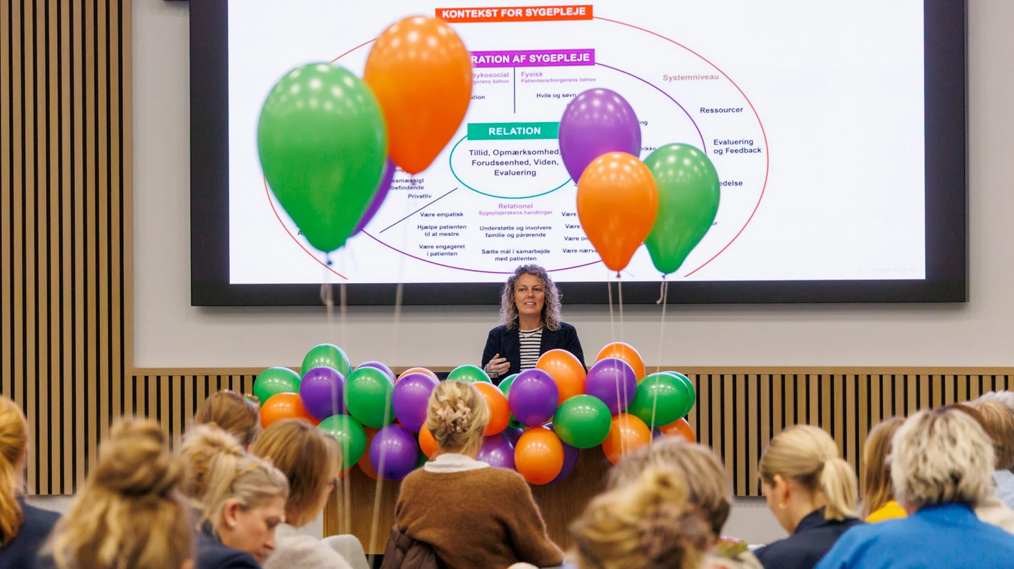 Kvinde på talerstol foran forsamling.