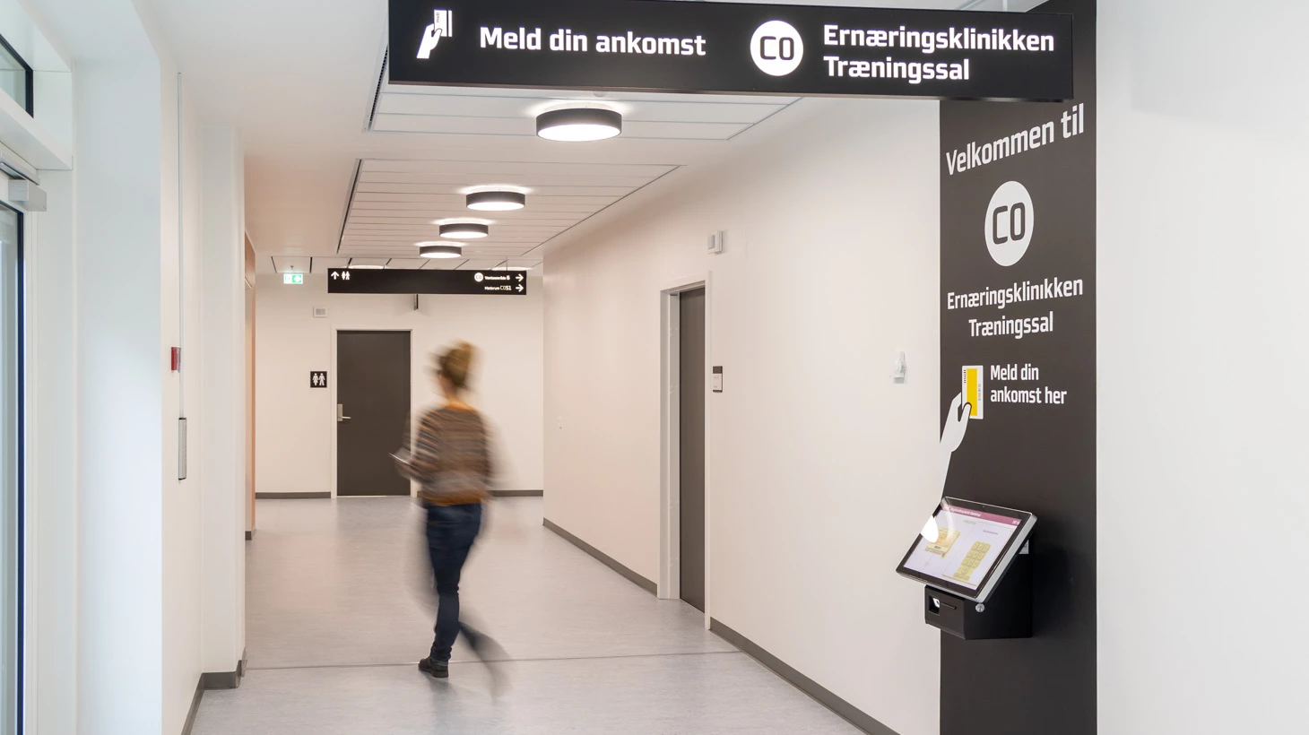 Hospitalsgang med skilte til Ernæringsklinikken og Træningssal og person der går.