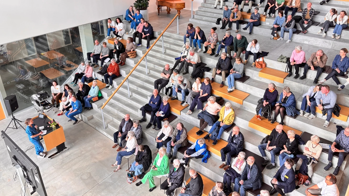 Stor gruppe deltagere der sidder på grå trappetrin indendørs.