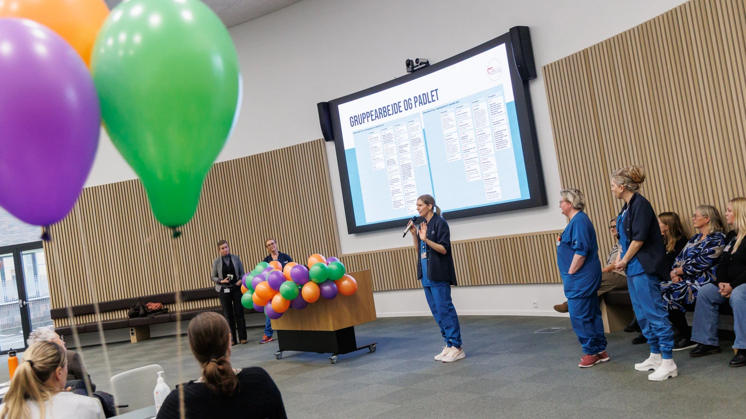 Kvinder taler foran forsamling  med balloner i forgrunden.