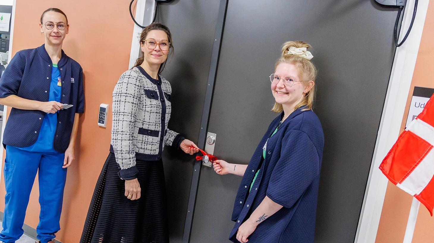 To kvinder i blå hospitalsuniform står med kvinde i civiltøj.