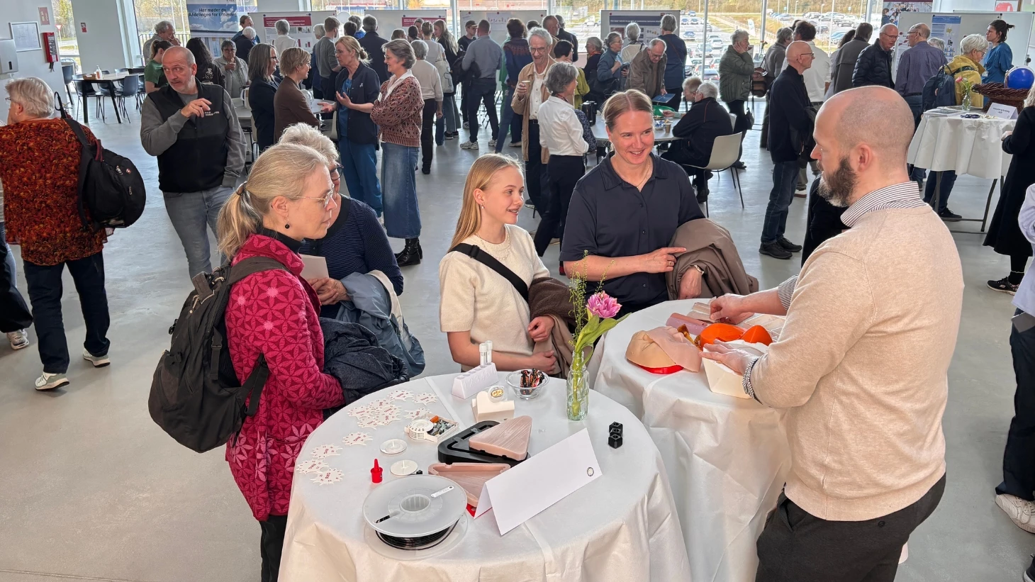 Fire mennesker omkring to runde borde i forgrunden. I baggrunden går mennesker forbi.