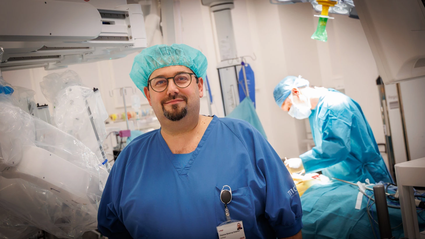 To personer på operationsstue iført blå hue og blå uniform