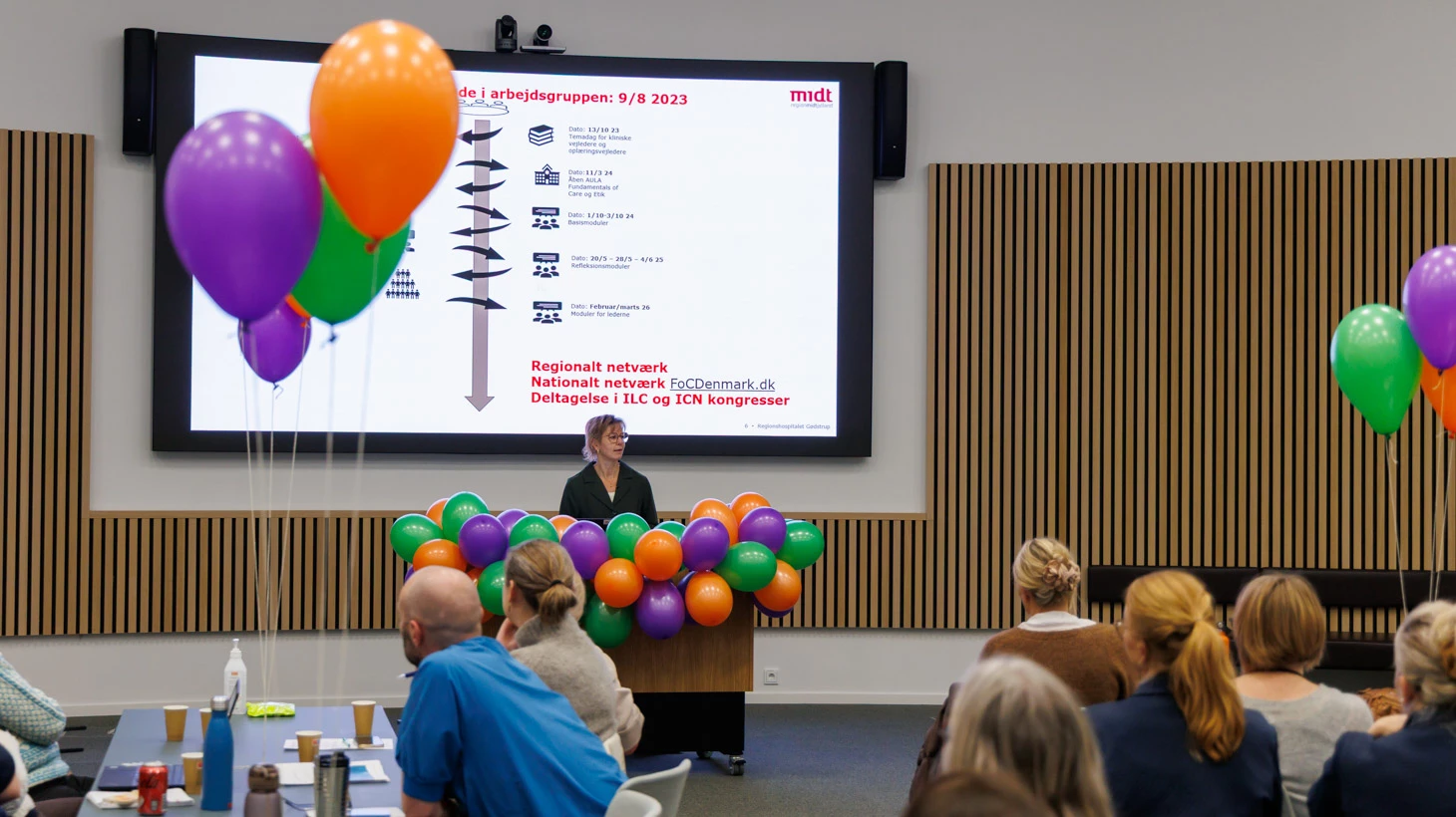 Kvinde på talerstol foran forsamling.