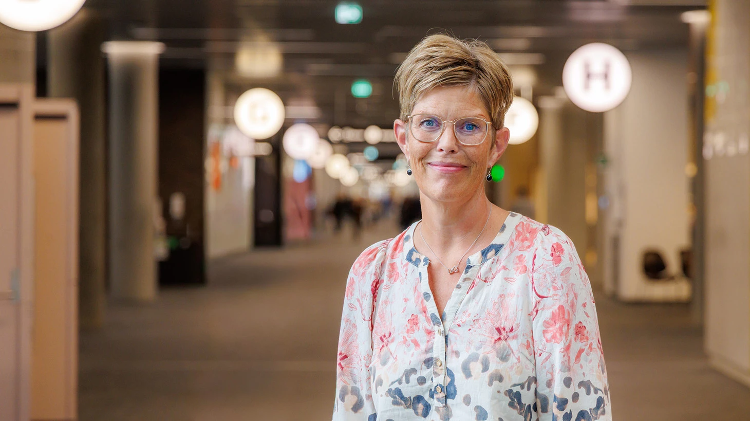 Foto af kvinde iført lys bluse og med hospitalsmiljø i baggrunden.