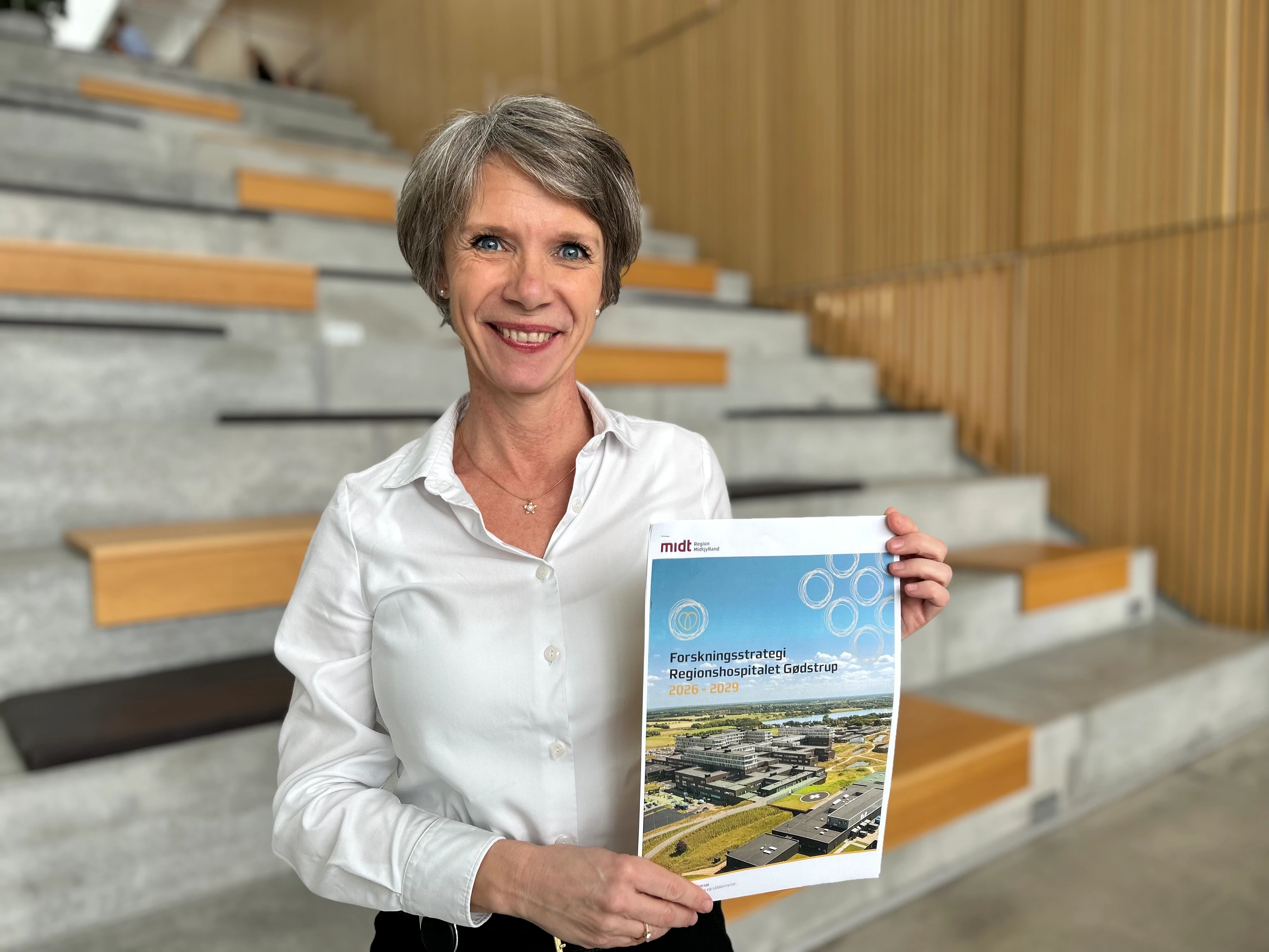 Kvinde i hvid skjorte holder farvet folder op foran grå trappe