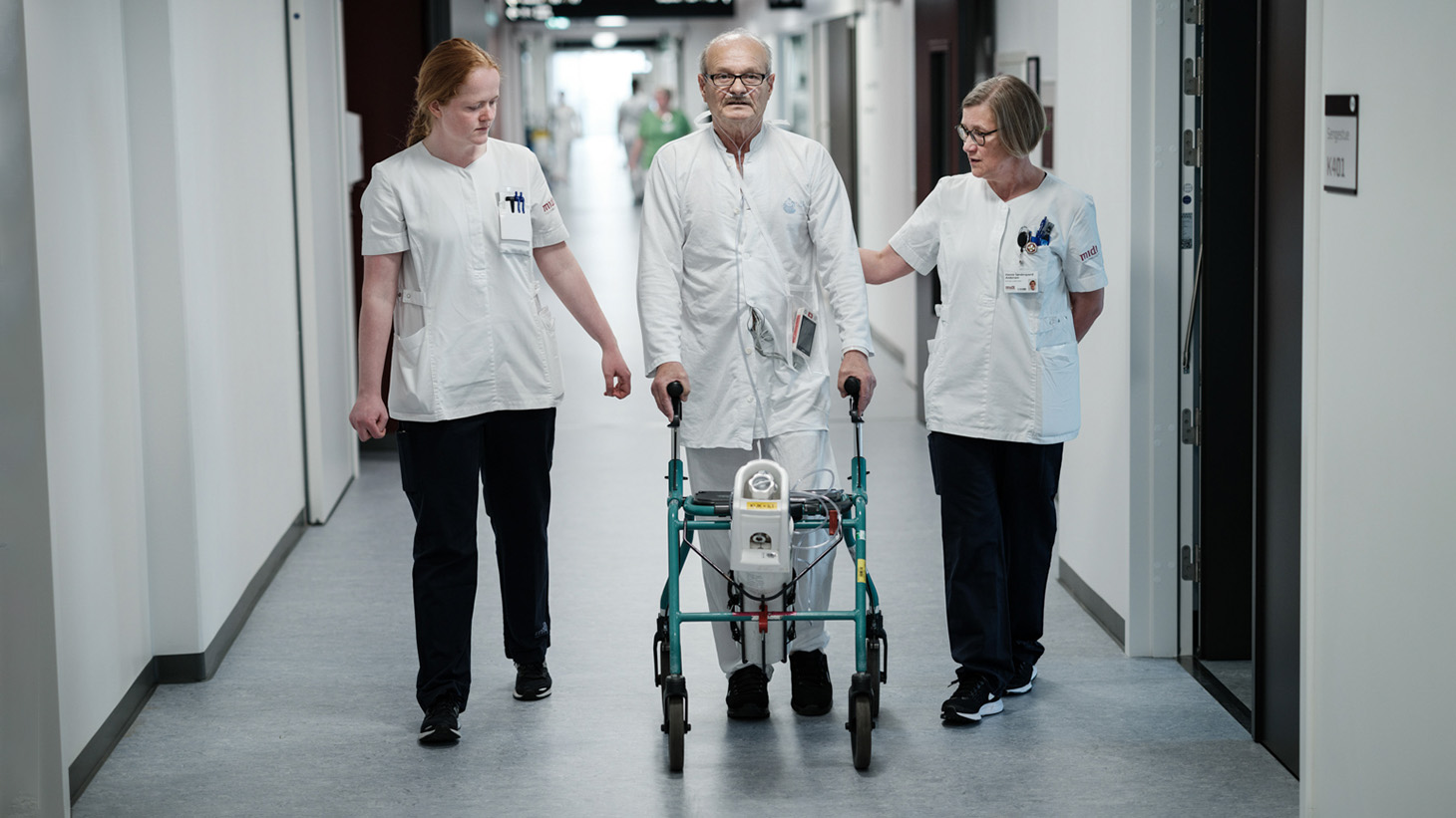 Fysioterapeuter støtter patient i at gå på gangen