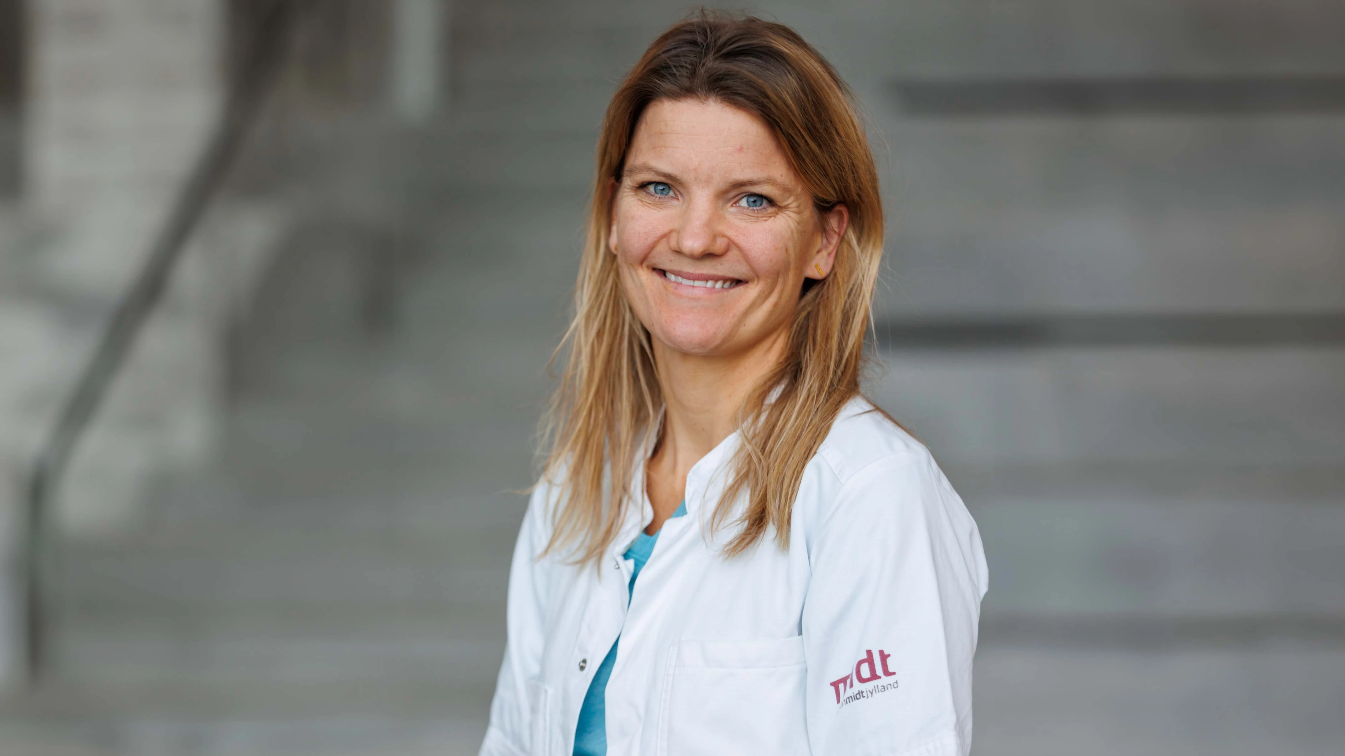 Kvinde i hvid lægekittel på grå baggrund.